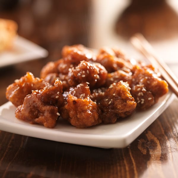 Close-up of Uncle Chung's Szechuan sesame chicken on a white plate with chopsticks.