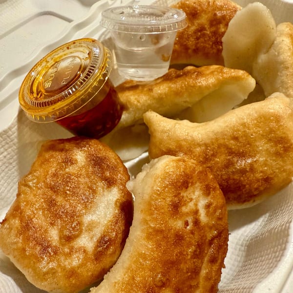 Golden-brown fried dumplings with chili oil and a small cup of sauce in a white takeout container.